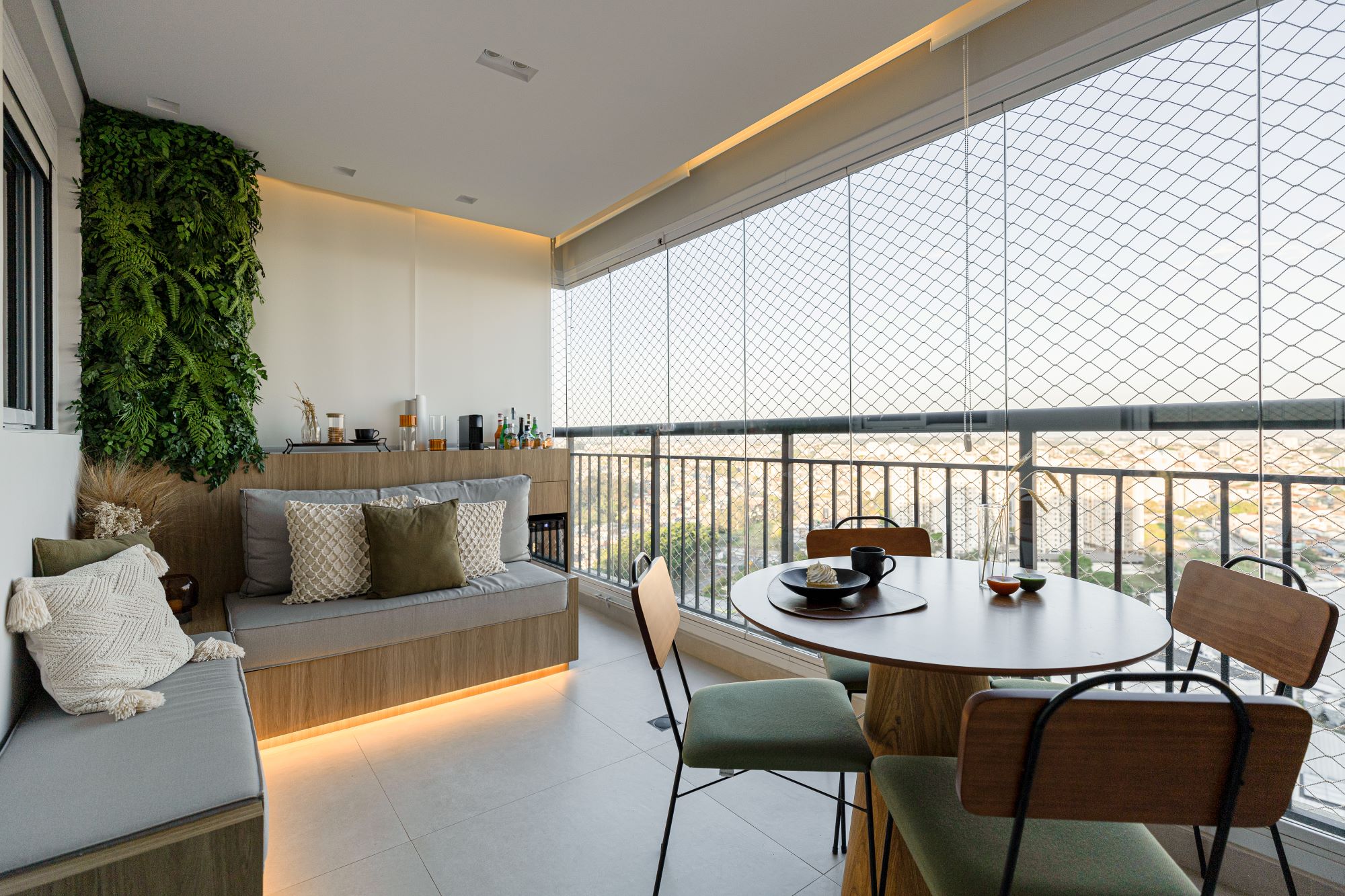 Projeto AB: varanda com jardim vertical, banco de madeira com luz embutida, mesa redonda e vista da cidade