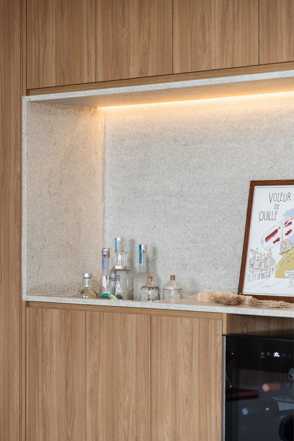 Projeto FF2: bar embutido na marcenaria de madeira, com nicho iluminado em pedra clara, garrafas, quadro e adega