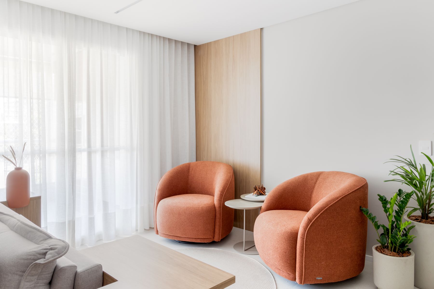 Projeto ES: duas poltronas terracota junto ao painel de madeira clara e à cortina translúcida
